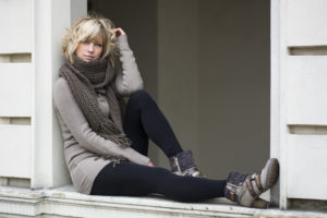 Attractive blonde young woman sitting on window sill, wearing winter clothes